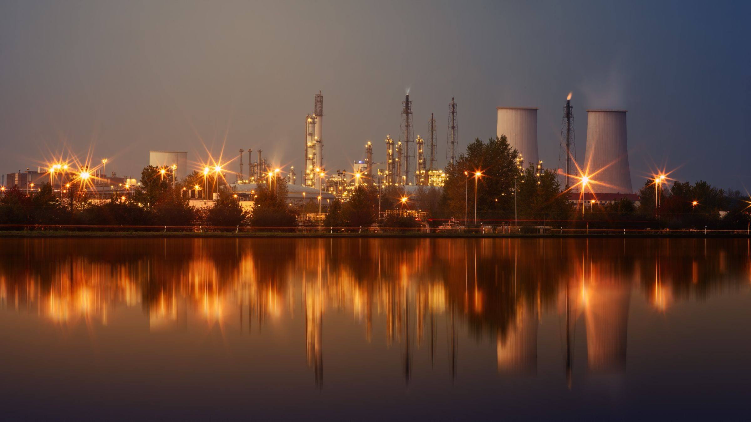 Oil refinery lit at dusk, reflected in water